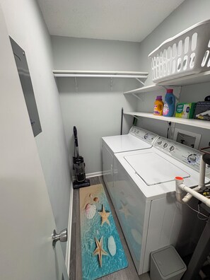 A laundry room with a washing machine, a vacuum cleaner, and shelves with cleaning supplies. - TOP-FLOOR WATERFRONT CONDO GETAWAY (Punta Gorda)