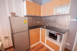 A compact kitchen with a refrigerator, microwave, sink, and wooden cabinets. - D603 Bright Cozy 2-bedroom apartment with Playground near Beach (Huahin)