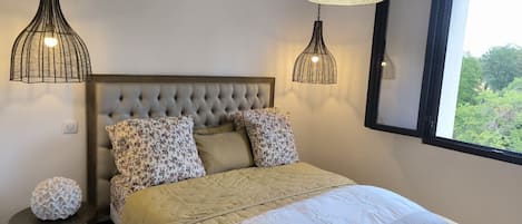A bedroom with a tufted headboard, floral pillows, a bed with a beige bedspread, and two pendant lights.