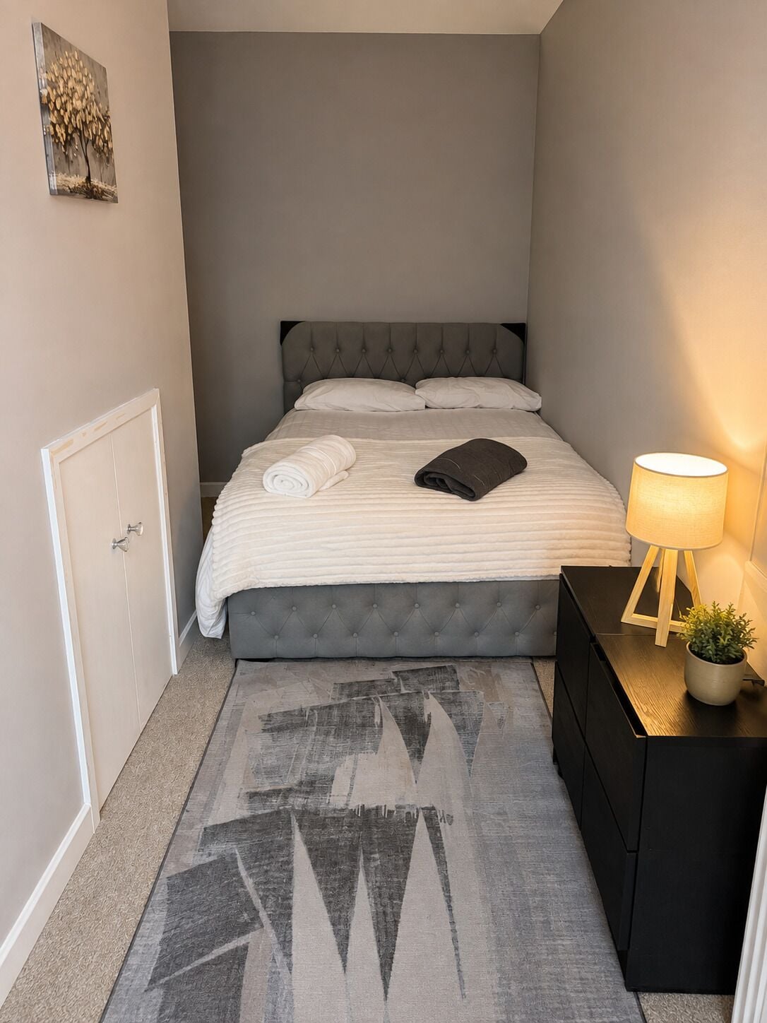 A neatly arranged bedroom with a bed, bedside table, lamp, and a small potted plant.