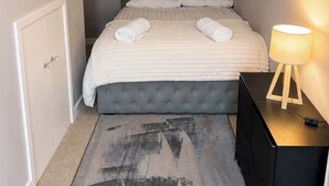A neatly made bed with a grey headboard, a bedside lamp, and a patterned rug. - Berwick - Close to Town, Bridges and Train Station (Berwick-upon-Tweed)