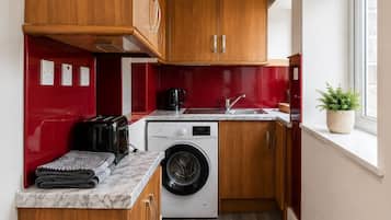 Une cuisine de taille réduite, avec des meubles de rangement en bois, un lave-linge, un grille-pain et un évier.