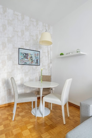 Ein Essbereich mit einem runden Tisch, zwei Stühlen, einer Pendelleuchte, einem gerahmten Kunstwerk an der Wand und einem weißen Regal mit Gegenständen.