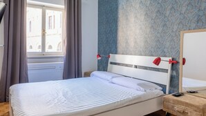 A bedroom with a bed, a nightstand, a red lamp, a wooden floor, and a window with curtains. - Charming suite with a view in the heart of Rome (Roma)
