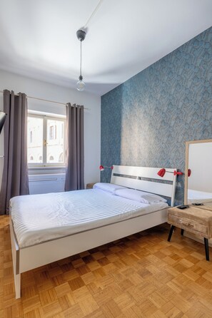 Ein Schlafzimmer mit einem Bett, einem Nachttisch, einer roten Lampe, Holzboden und einem Vorhangfenster.