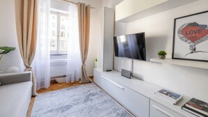 A modern living room with a flat-screen TV, a sofa, a coffee table, and a bookshelf with books and a framed picture. - Charming suite with a view in the heart of Rome (Roma)