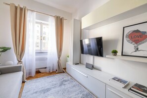 Ein modernes Wohnzimmer mit Flachbildfernseher, einer Couch, einem Couchtisch und einem Bücherregal mit Büchern und einem gerahmten Bild.