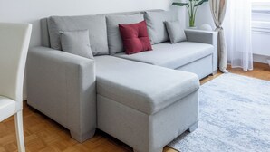 A modern living room with a grey sectional sofa, a red accent pillow, a white armchair, a grey pendant light, and a large abstract painting on the wall. - Charming suite with a view in the heart of Rome (Roma)
