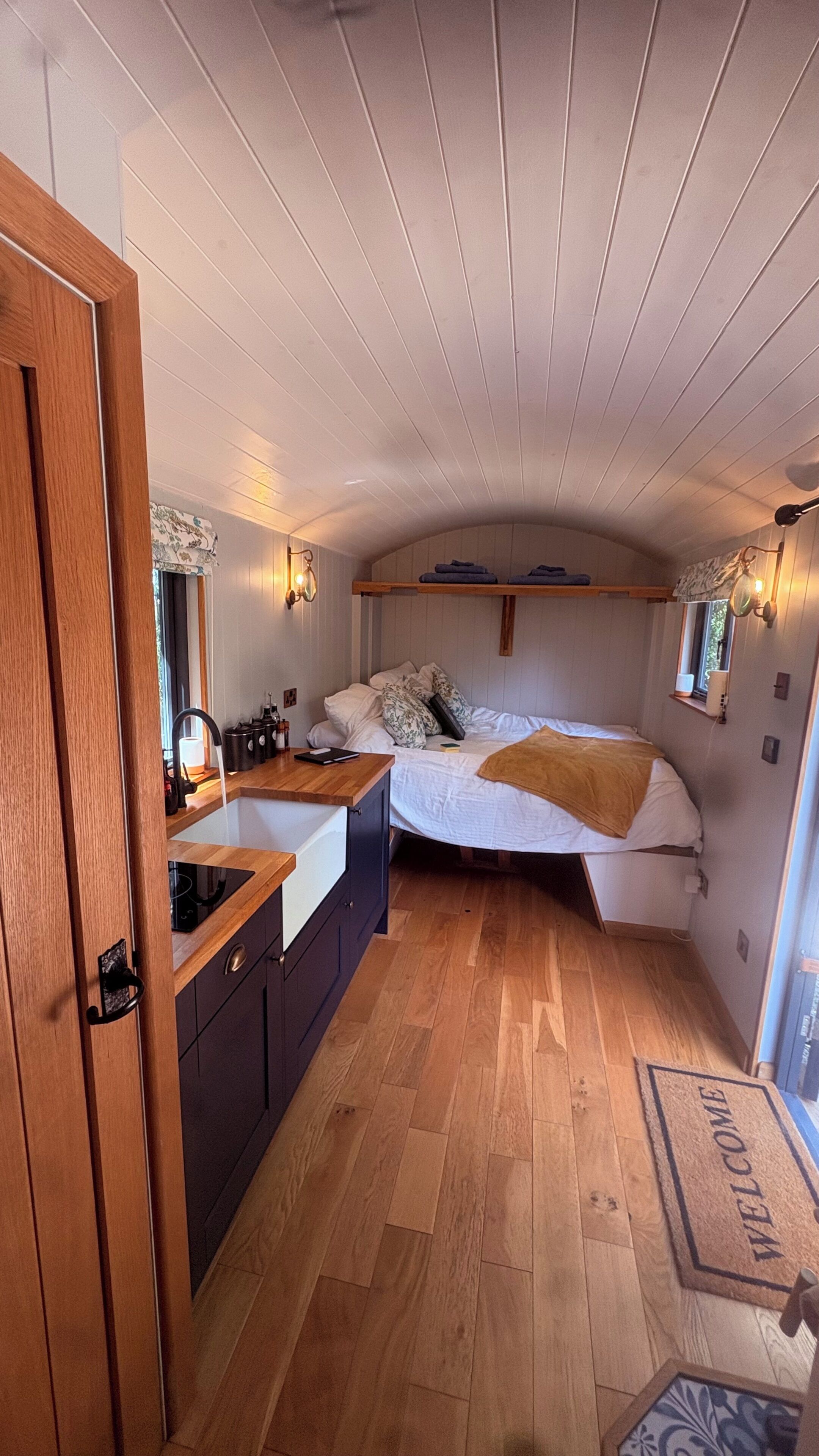 A compact bedroom with a bunk bed, a small bedside table, a built-in bench, and a window with curtains.