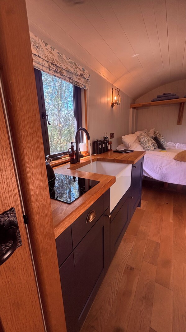 A compact kitchen with a wooden countertop, a sink, and a window with a view of trees.