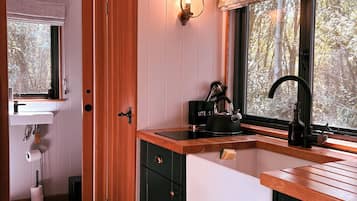 A kitchen with wooden cabinets, a black kettle, and a window with a view of trees.
