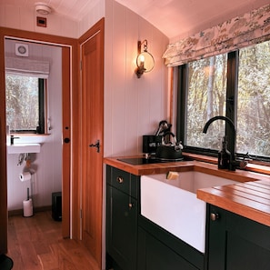 A kitchen with wooden cabinets, a black kettle, and a window with a view of trees.