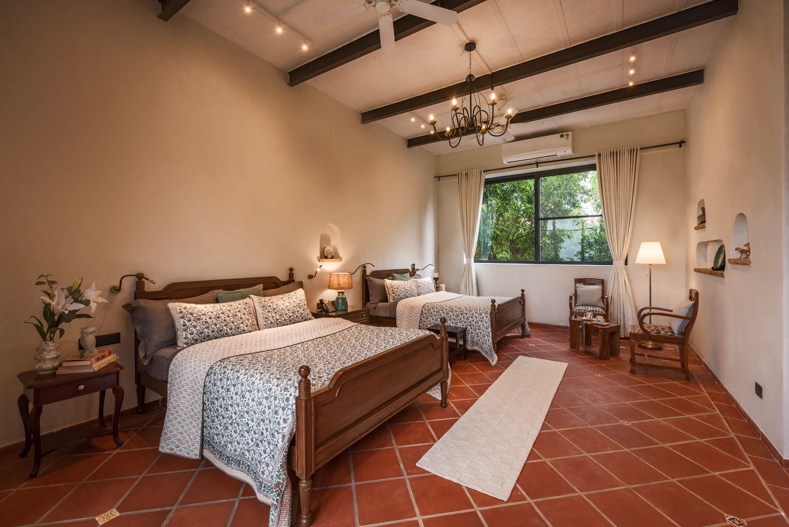 A bedroom with two wooden beds, a large window with curtains, a chandelier, and a tiled floor.