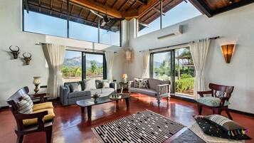 A spacious living area with a high ceiling, large windows, and a view of the outdoors.