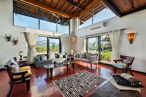 A spacious living area with a high ceiling, large windows, and a view of the outdoors.