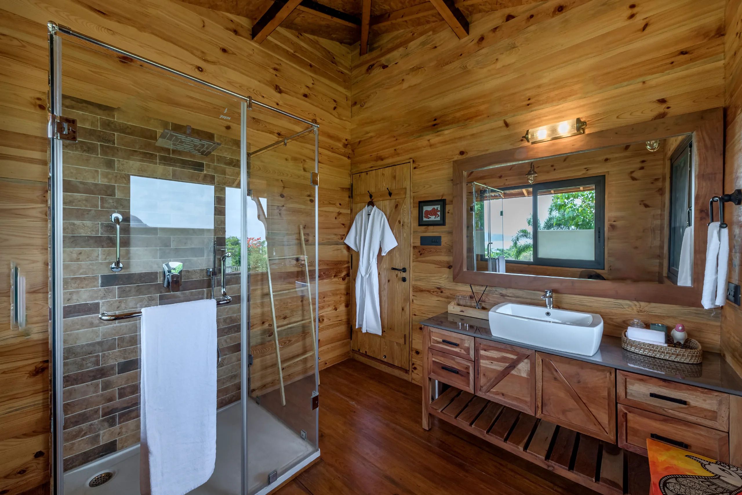 Un baño de cabaña de madera con mampara de vidrio, lavabo y tocador.