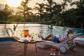 A poolside setting with a table set for drinks, a lounge chair, and a volleyball net. - Satori Mulshi (Paud)