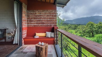 Un balcón con un sofá rojo, un taburete de madera y vistas a exuberante follaje y montañas.