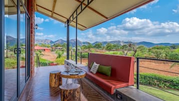 A balcony with a red sofa, a wooden table, and a view of mountains.