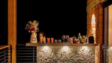 A bar area with a rustic stone counter, a vase of flowers, candles, and various glasses and bottles.