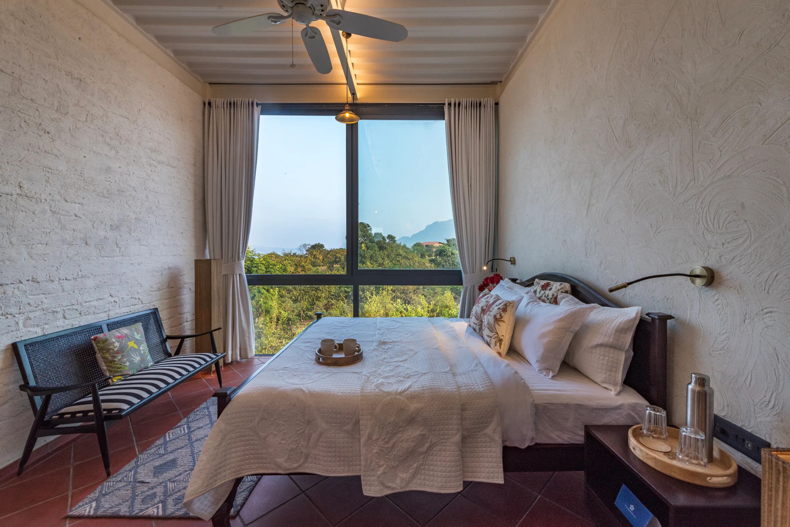 Un dormitorio con cama, una silla, mesita de noche y vistas al exterior.