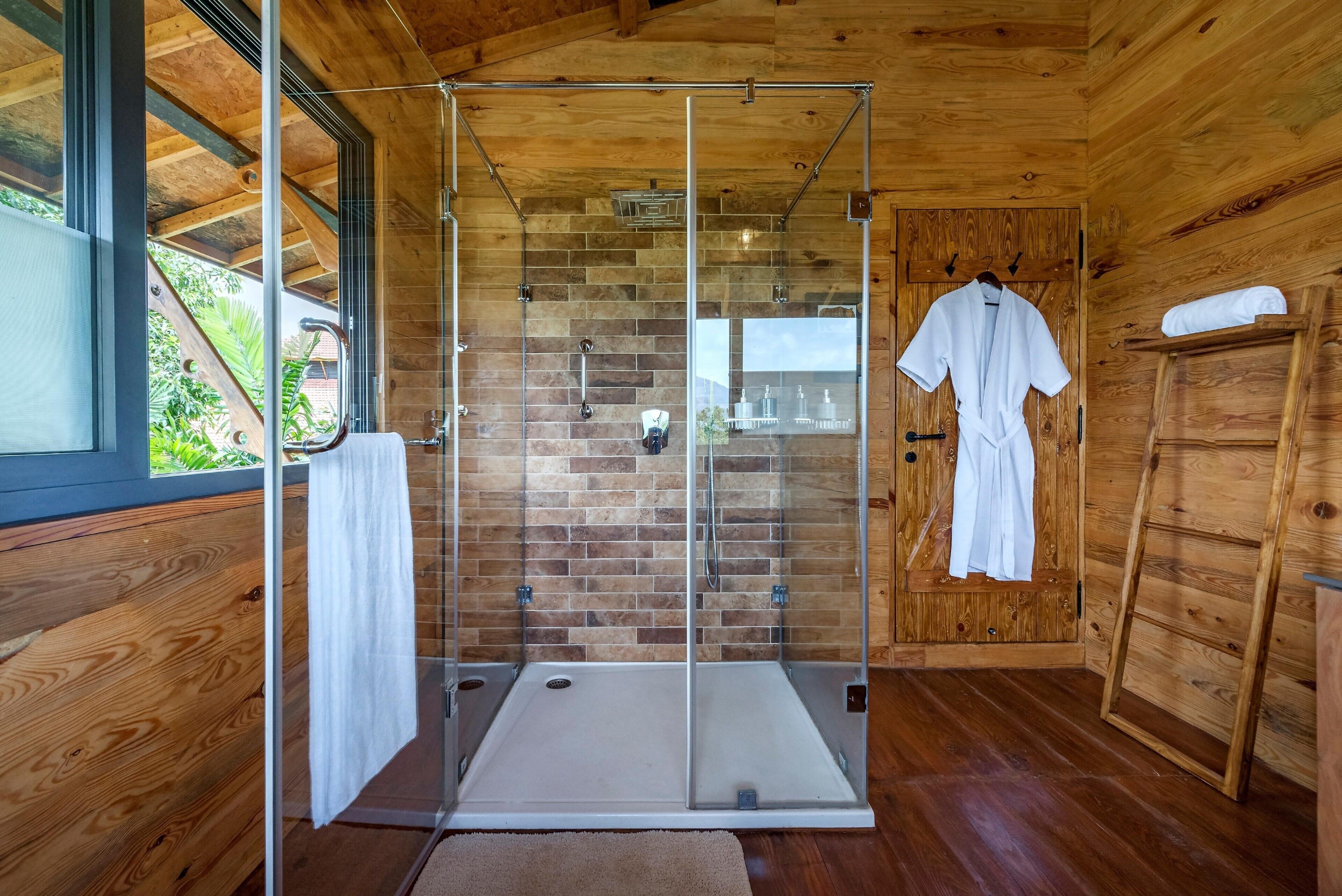 A modern bathroom with a glass-enclosed shower, wooden walls, and a wooden door with a towel rack.