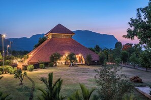A large, pyramid-shaped building with a red roof, surrounded by a well-maintained garden and a mountainous backdrop.
