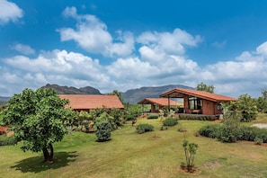 A two-story building with a red-tiled roof, surrounded by lush greenery and mountains in the background.