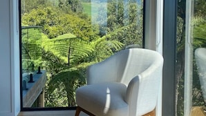 Een kamer met een grote schuifdeur naar een balkon, met uitzicht op een groen landschap en heuvels.