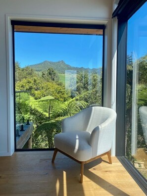 Ein Zimmer mit einer großen Schiebeglasdoor, die auf einen Balkon mit Blick auf eine grüne Landschaft und Hügel führt.
