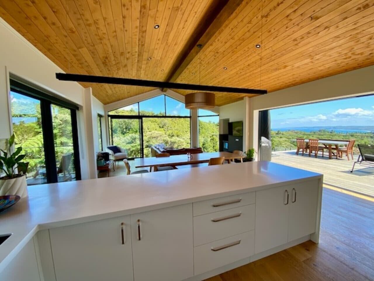A modern kitchen with a large island, wooden ceiling, and a view of the outdoors.