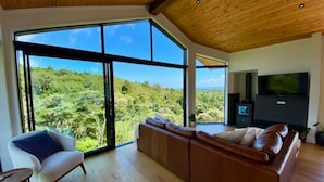 Een moderne woonkamer met een groot raam, een bank, een fauteuil en een flatscreen televisie.