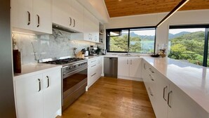 Een moderne keuken met witte kasten, een roestvrijstalen fornuis en uitzicht op het buitenleven door grote ramen.