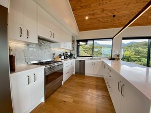 Eine moderne Küche mit weißen Schränken, einem Edelstahlherd und Blick ins Freie durch große Fenster.