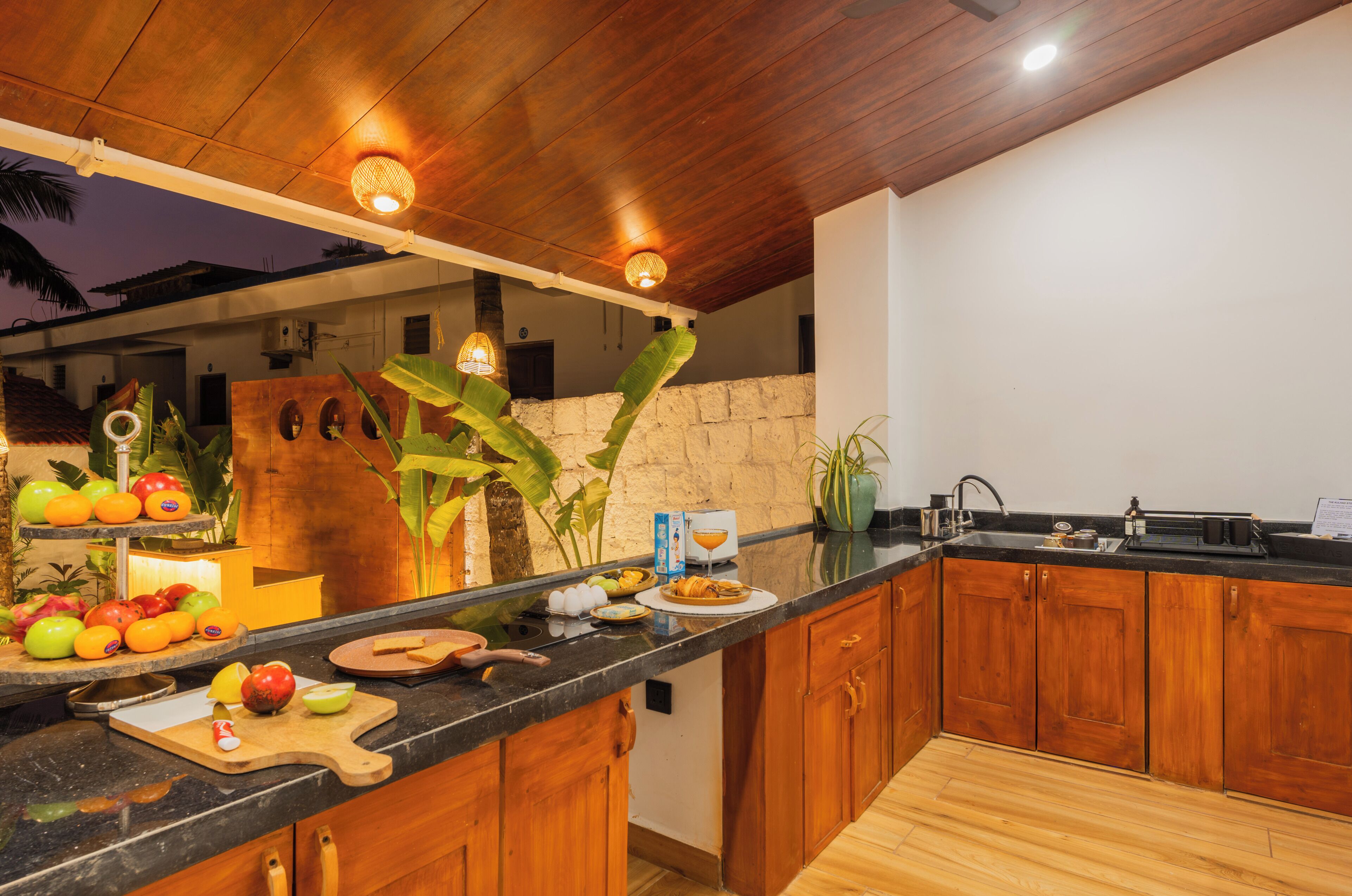 A kitchen with wooden cabinets, a black countertop, and a stone wall.
