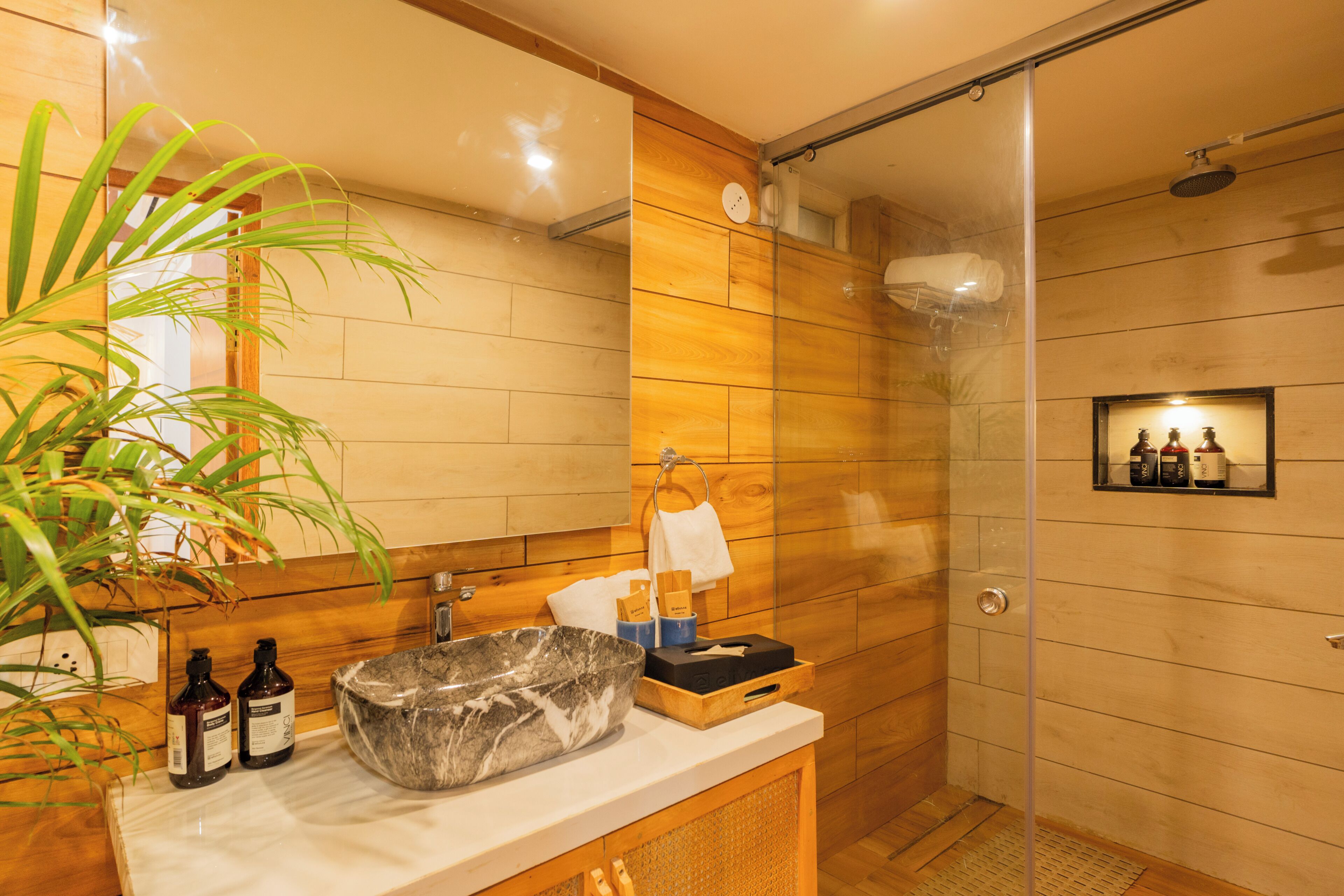 Un baño moderno con tocador de madera, un lavabo grande y mampara de ducha de vidrio.