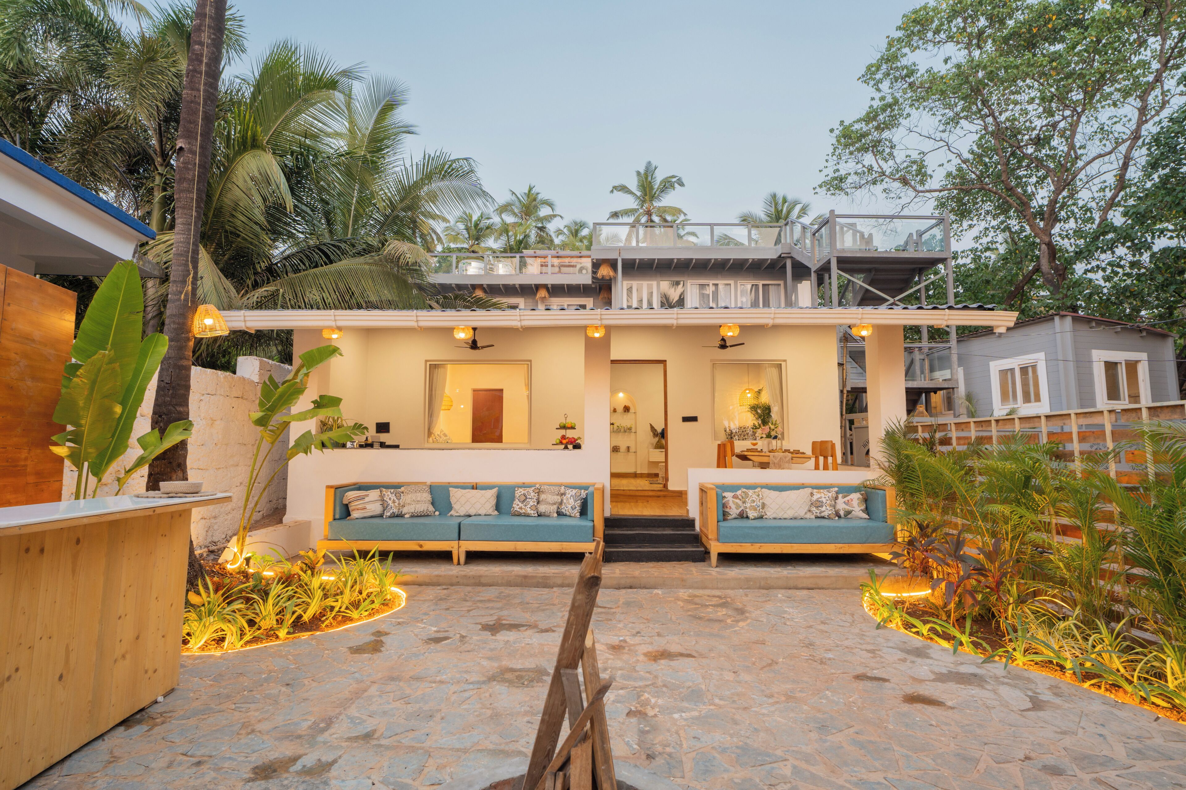 A modern house with a stone-paved entrance, a wooden reception desk, and two blue sofas with cushions.