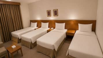 A hotel room with four single beds, a small table, a chair, and two framed pictures on the wall.