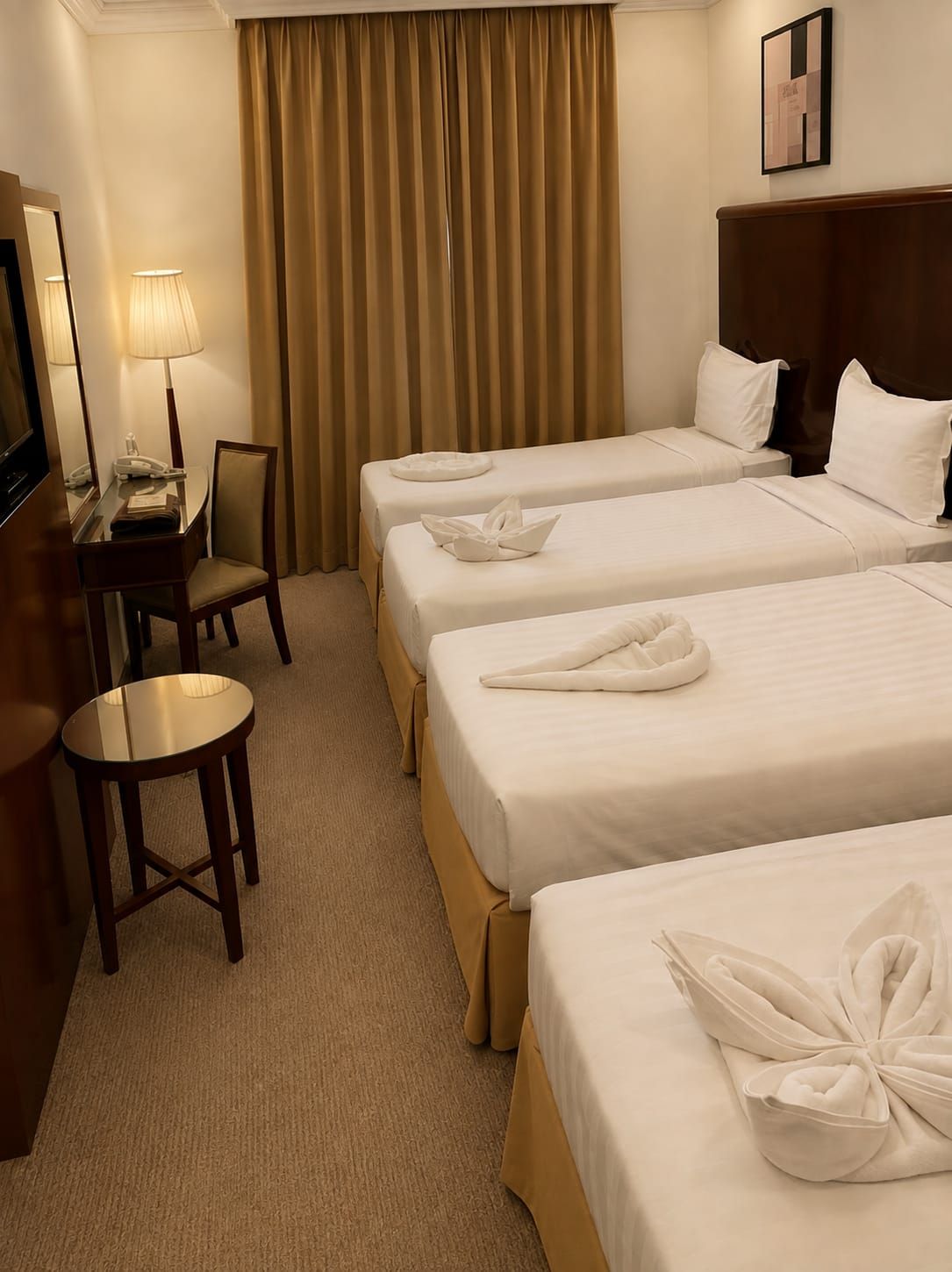 Een hotelkamer met drie bedden, een bureau met lamp, een stoel en een televisie.