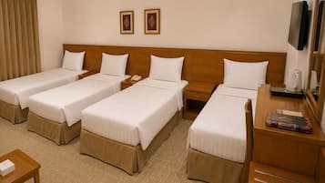 Een hotelkamer met vier eenpersoonsbedden, een houten hoofdeinde, een bureau met een stoel, een televisie en een klein tafeltje met een boek.