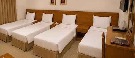 A hotel room with four single beds, a wooden headboard, a desk with a chair, a television, and a small table with a book.