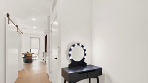 En hall med ett sminkbord och en spegel med belysning, som leder in till ett rum med ett matbord och stolar.