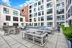 Eine Dachterrasse mit Außenmöbeln, einem Pool und einem modernen Gebäude mit mehreren Balkonen.