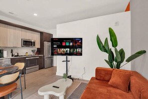 Ein modernes Wohnzimmer mit einem Flachbildfernseher, der eine Streaming-Dienstanwendung zeigt, einem Sofa, einem Couchtisch und einer großen Pflanze.