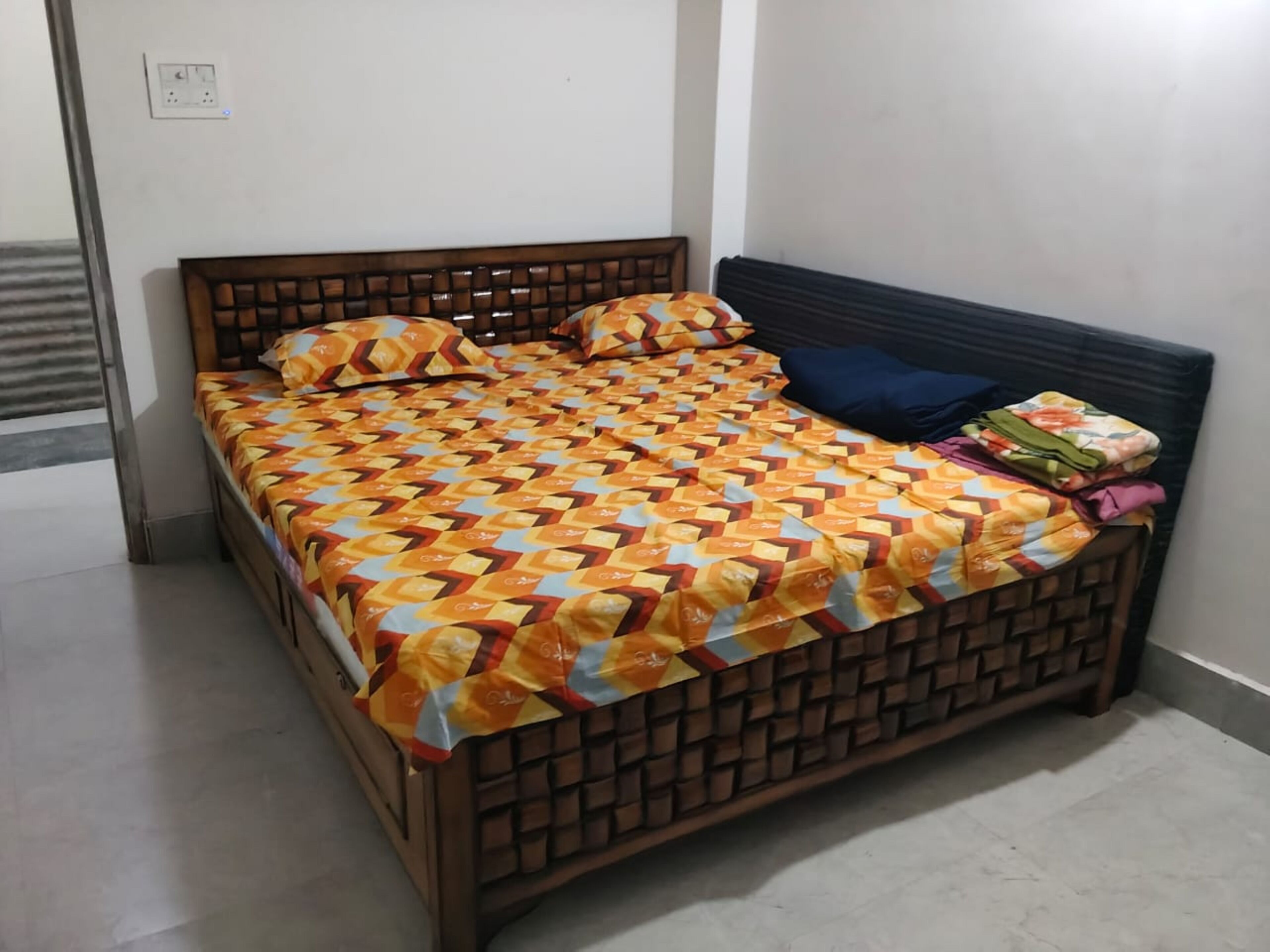 Uma cama com colcha estampada, cabeceira e travesseiro sobre um chão de azulejos.