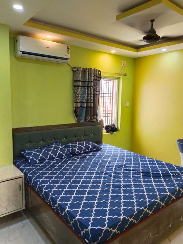 A bedroom with a bed, a window with curtains, an air conditioner, and a ceiling fan.