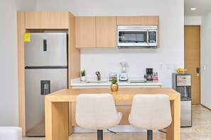 Eine moderne Küche mit Kühlschrank, Mikrowelle, Kaffeemaschine und Mixer. Ein Holztisch mit zwei Stühlen und einer kleinen Pflanze steht daneben.