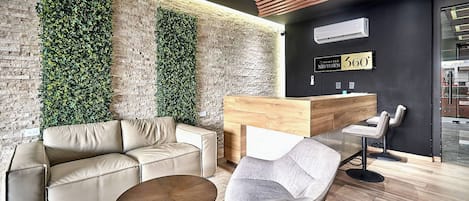 A modern reception area with a wooden reception desk, a leather sofa, a grey armchair, and a round coffee table.