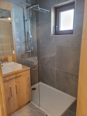Ein modernes Badezimmer mit einer gläsernen Dusche, einem Holzwaschtisch und einem kleinen Fenster.