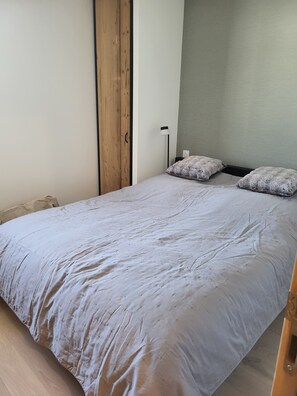 Una cama individual con edredón gris, un armario de madera y una lámpara de noche.